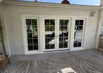 Three elegant glass doors with white frames open to a patio, surrounded by a patterned rug and a clear blue sky above.