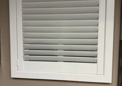 A closed white plantation shutter window with horizontal slats, set against a beige wall.
