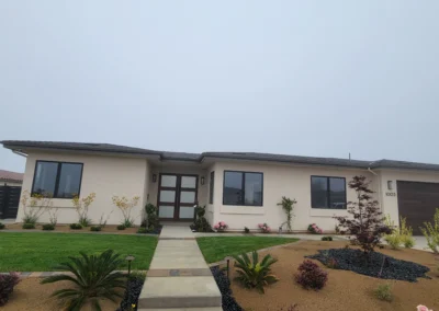 Modern home with a light exterior, large windows, landscaped garden, and a paved walkway beneath a cloudy sky.